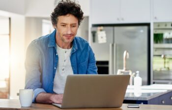 Man, laptop or typing in kitchen for remote work, web designer with check for schedule. Male entrepreneur, computer or reading in home for creative development, digital administration with technology